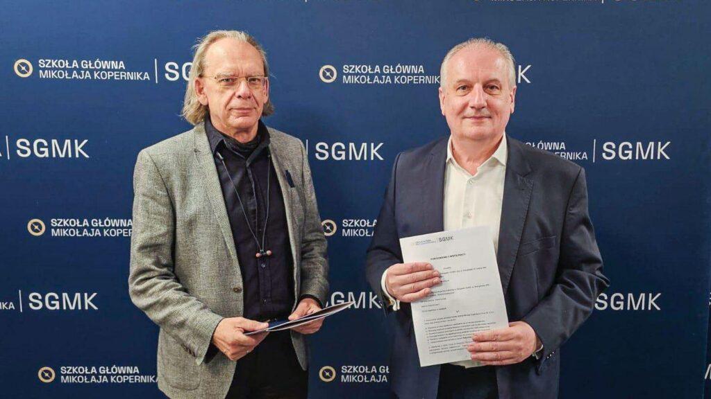 Dwaj mężczyźni stojący przed ścianą z logo Szkoły Głównej Mikołaja Kopernika. Obaj trzymają dokumenty; mężczyzna po prawej, lekko uśmiechnięty, prezentuje widoczne porozumienie o współpracy.