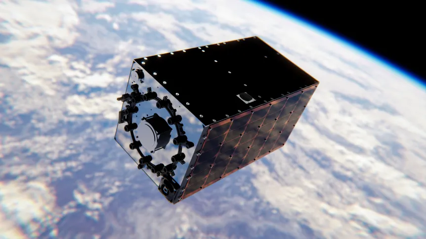 Satelita w kształcie sześcianu, z ciemnymi i odblaskowymi bokami oraz panelami słonecznymi, orbitujący nad Ziemią pokrytą chmurami, z widoczną błękitną linią atmosfery na tle czarnej przestrzeni kosmicznej.