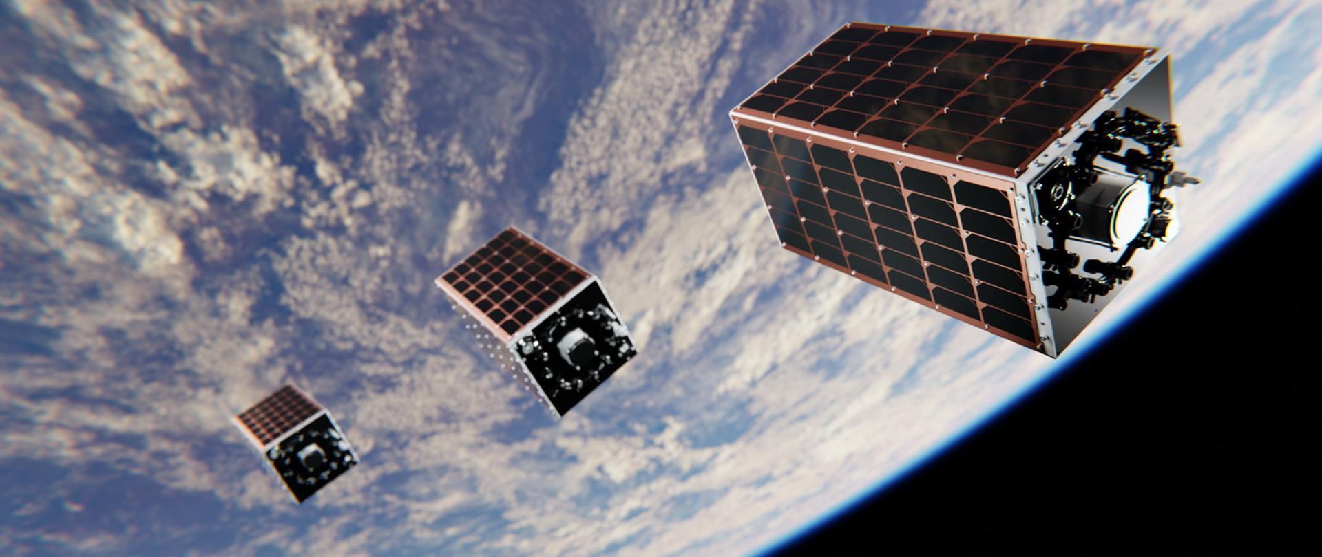 Trzy satelity z panelami słonecznymi, ułożone w formacji, krążą nad Ziemią. Najbliższy z nich jest szczegółowo widoczny, ukazując oprzyrządowanie pomiarowe. W tle rozpościera się błękitna warstwa atmosfery, białe chmury oraz czerń kosmosu.