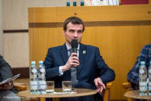 Mężczyzna w garniturze przemawia do mikrofonu podczas panelu dyskusyjnego.