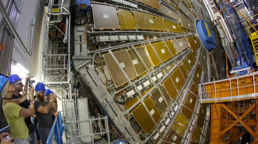 Osoby w kaskach fotografują gigantyczny detektor cząstek elementarnych w laboratorium.