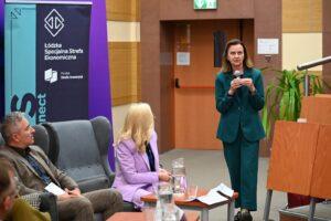 Prof. Gertruda Uścińska w zielonym garniturze przemawia do mikrofonu podczas spotkania Łódzkiej Specjalnej Strefy Ekonomicznej.