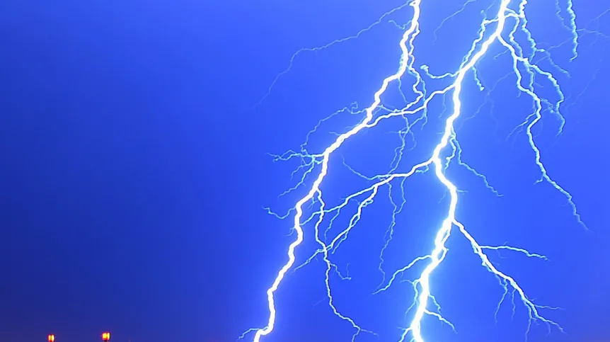 Rozgałęziony, jasny piorun na tle ciemnoniebieskiego nocnego nieba.