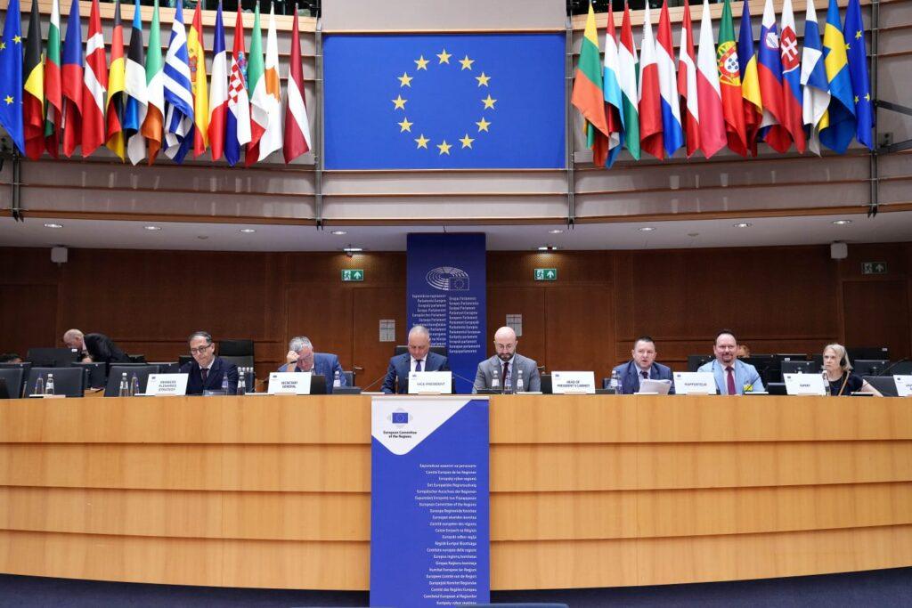 Obrady Europejskiego Komitetu Regionów. Panelistowie przy stole pod flagami państw członkowskich UE.