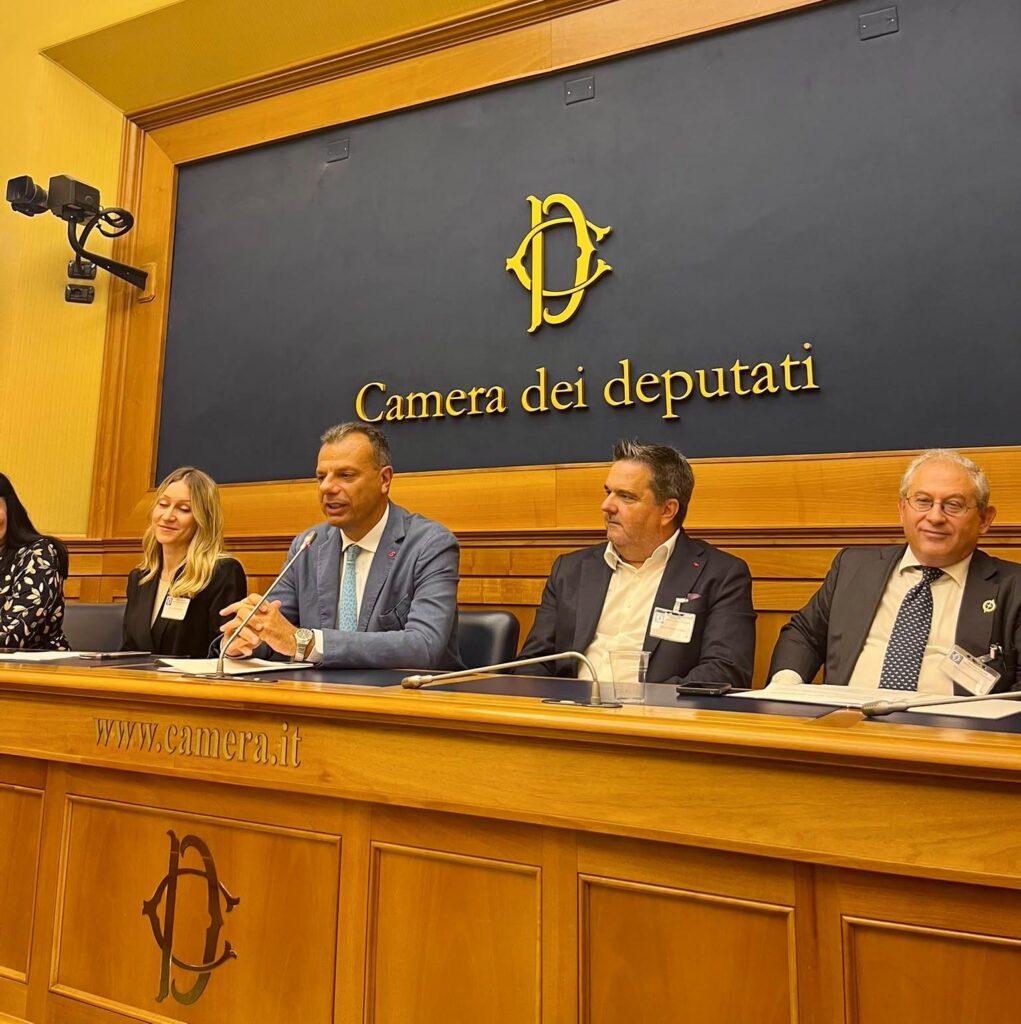 Panel dyskusyjny w Camera dei deputati. Czworo panelistów siedzi za stołem, jeden z nich przemawia.